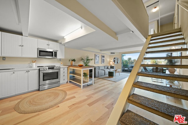 kitchen featuring rail lighting, beam ceiling, appliances with stainless steel finishes, light hardwood / wood-style floors, and white cabinetry