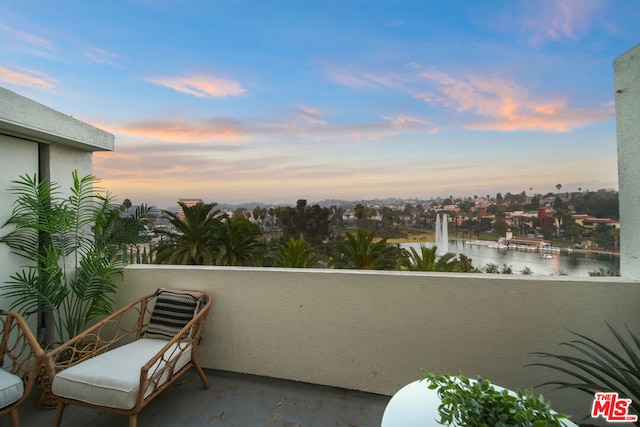 balcony at dusk featuring a water view