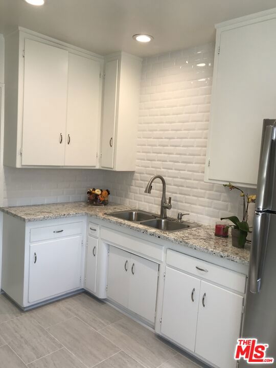 kitchen featuring white cabinets, sink, tasteful backsplash, light stone counters, and stainless steel refrigerator