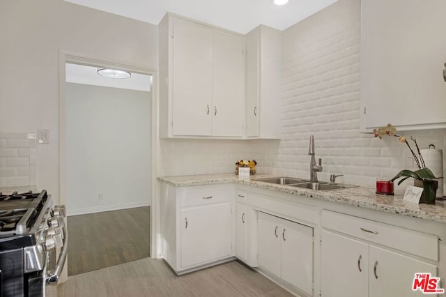 kitchen featuring high end range, sink, decorative backsplash, light stone counters, and white cabinetry