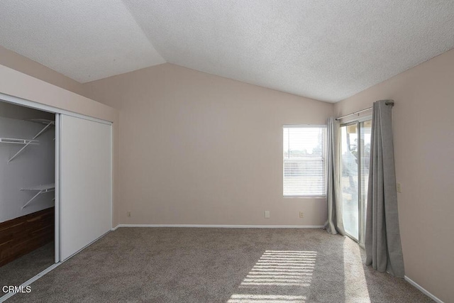 unfurnished bedroom featuring carpet, a textured ceiling, vaulted ceiling, and a closet