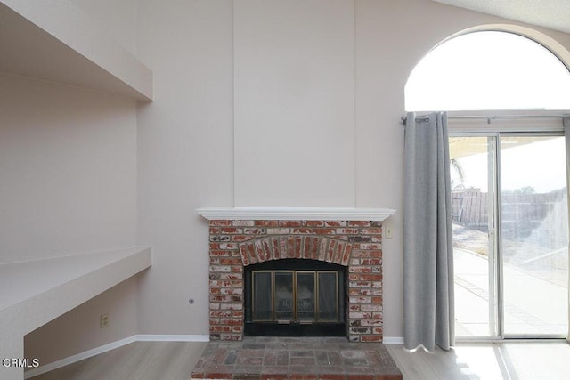 unfurnished living room with wood-type flooring and a brick fireplace