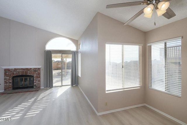 unfurnished living room with light wood-type flooring, a brick fireplace, a textured ceiling, ceiling fan, and lofted ceiling