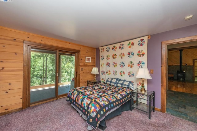 carpeted bedroom featuring wood walls, access to exterior, and a wood stove