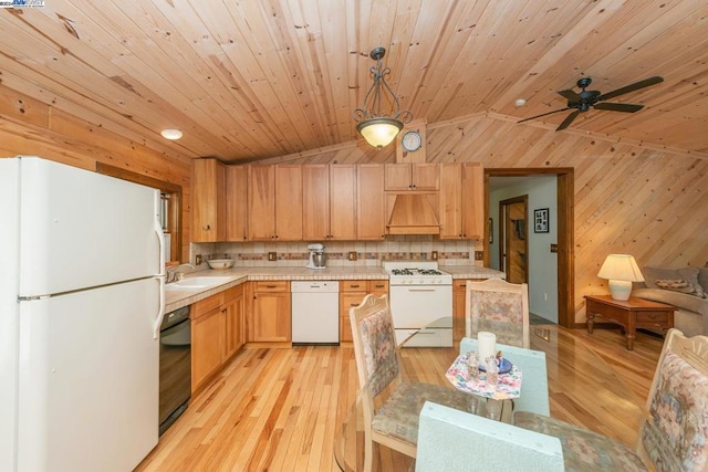 kitchen featuring white appliances, wooden walls, vaulted ceiling, decorative light fixtures, and custom range hood