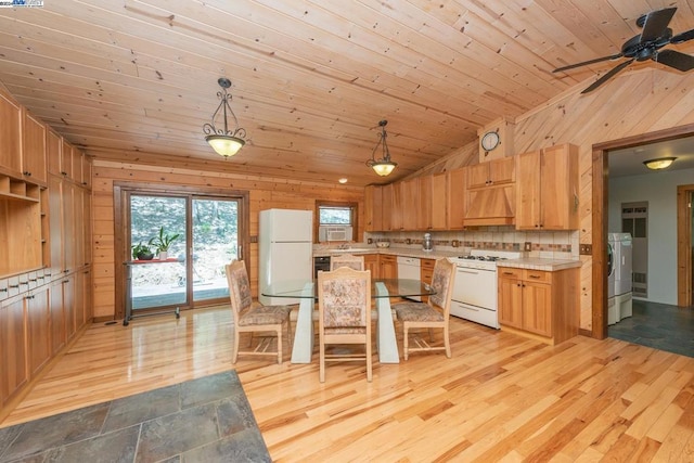 kitchen with custom exhaust hood, wood walls, white appliances, hanging light fixtures, and light hardwood / wood-style flooring