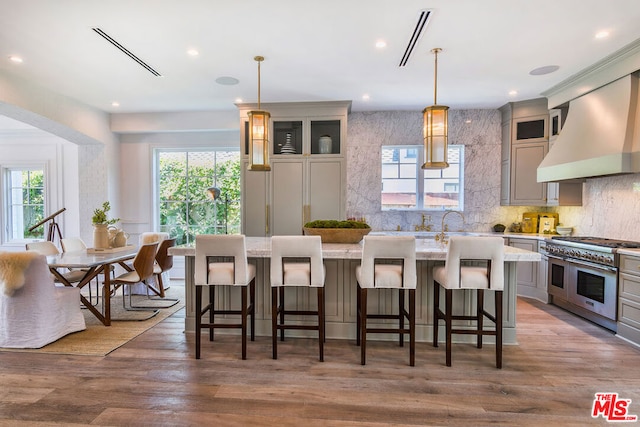 kitchen with decorative light fixtures, a kitchen island with sink, range with two ovens, and custom range hood