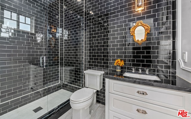 bathroom featuring toilet, vanity, tile walls, tile patterned floors, and a shower with door