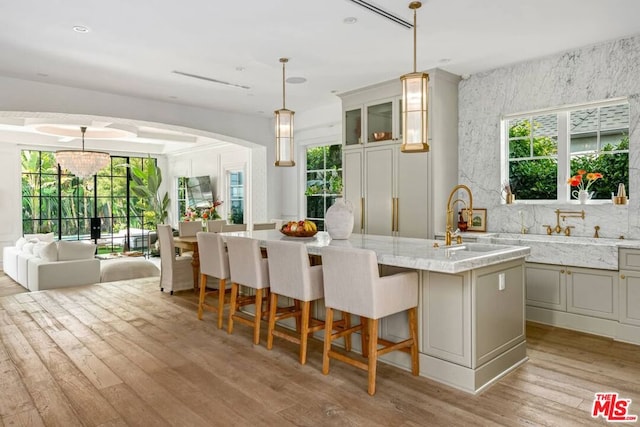 kitchen featuring decorative light fixtures, sink, a kitchen island with sink, light stone countertops, and light wood-type flooring