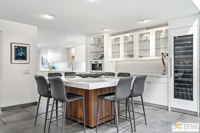 interior space with a kitchen island, wine cooler, a breakfast bar area, decorative backsplash, and white cabinets