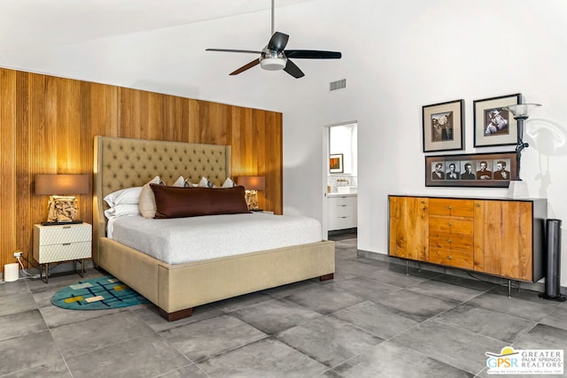 bedroom featuring wooden walls, ceiling fan, high vaulted ceiling, and ensuite bath