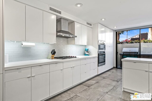 kitchen with white cabinets, appliances with stainless steel finishes, tasteful backsplash, and wall chimney range hood