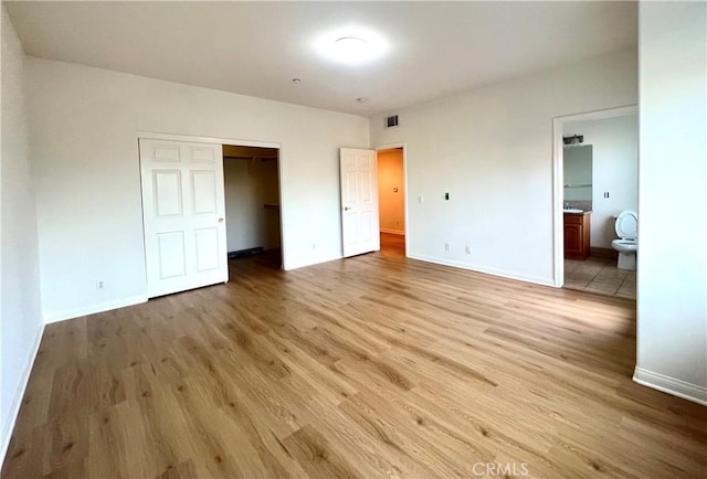 unfurnished bedroom with light hardwood / wood-style floors, a walk in closet, a closet, and ensuite bath