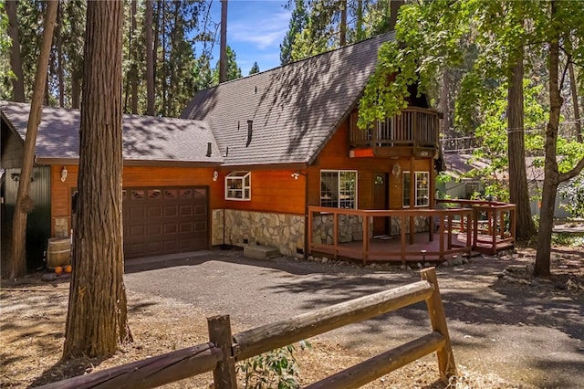 rear view of property with a garage, a shingled roof, stone siding, gravel driveway, and a wooden deck