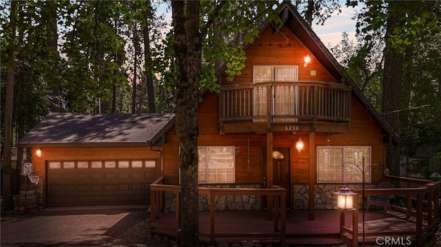 view of front of property with stone siding, an attached garage, and a balcony