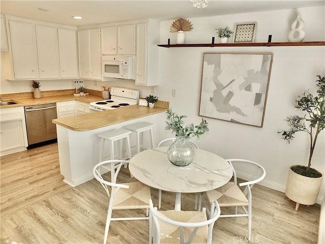 kitchen featuring kitchen peninsula, light wood-type flooring, white appliances, and white cabinets