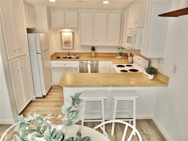 kitchen featuring white appliances, sink, kitchen peninsula, light hardwood / wood-style flooring, and white cabinetry