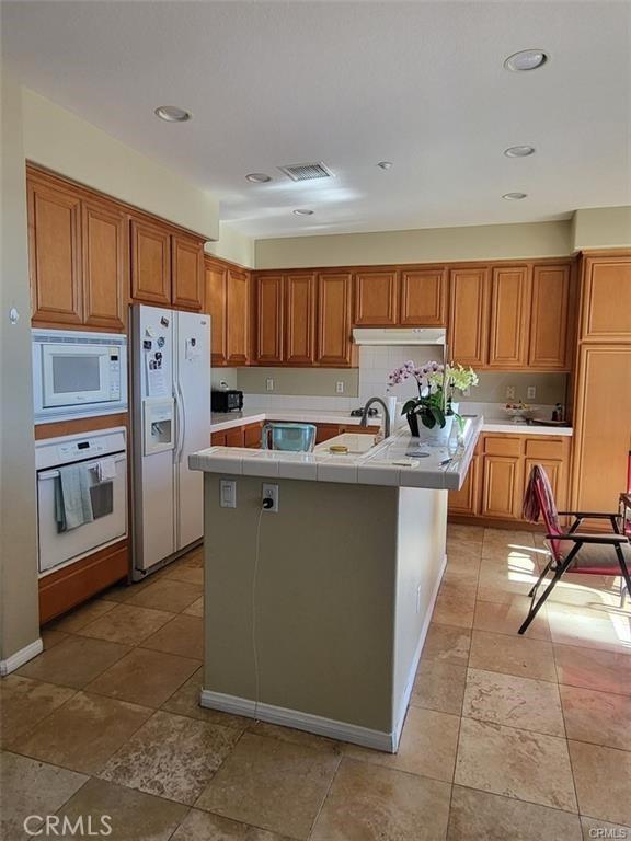 29367 Lytle Ln, Highland, CA 92346 - kitchen with visible vents, white appliances, tile counters, brown cabinetry, and a center island with sink