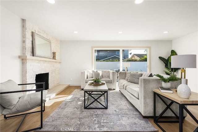 living area featuring baseboards, a stone fireplace, wood finished floors, and recessed lighting