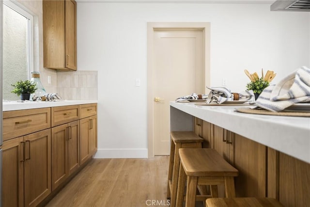 kitchen with a kitchen breakfast bar, light countertops, decorative backsplash, brown cabinets, and light wood finished floors