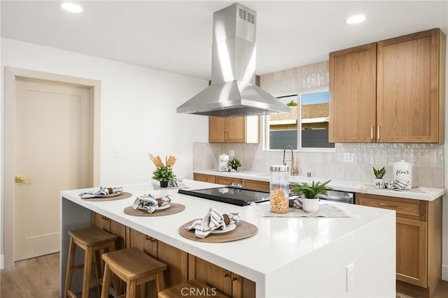 kitchen featuring a breakfast bar area, island range hood, a center island, light wood-type flooring, and backsplash