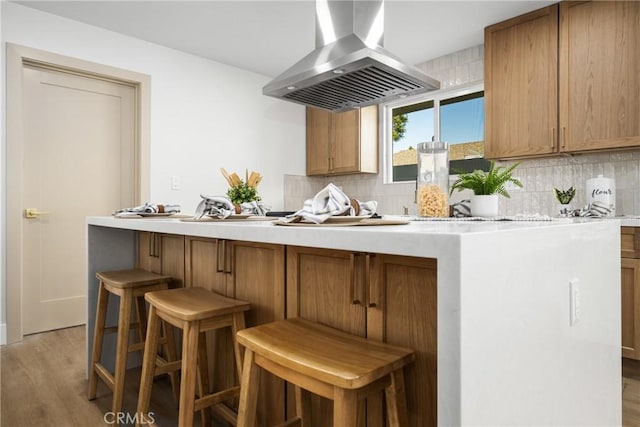 kitchen with light wood-type flooring, tasteful backsplash, island range hood, and light countertops