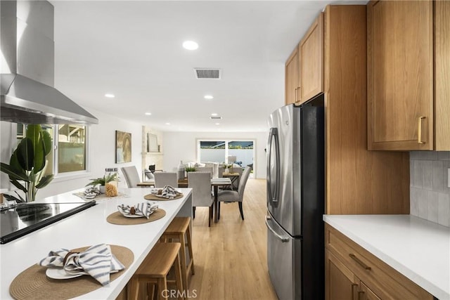 kitchen featuring a breakfast bar, light wood-type flooring, stainless steel refrigerator, island exhaust hood, and backsplash