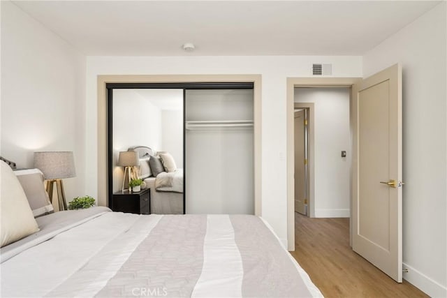 bedroom with a closet, wood finished floors, visible vents, and baseboards