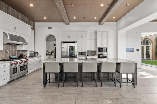 kitchen with beam ceiling, a large island with sink, built in appliances, and a breakfast bar area