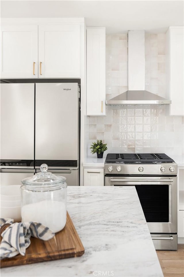 kitchen with tasteful backsplash, white cabinets, fridge, gas range, and wall chimney range hood