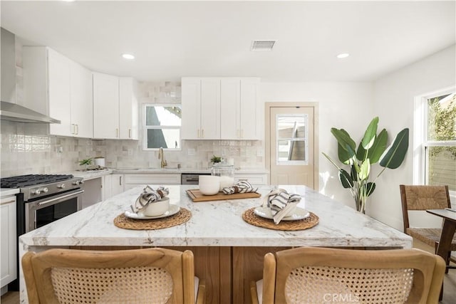 kitchen with white cabinetry, a kitchen island, wall chimney range hood, and high end stove