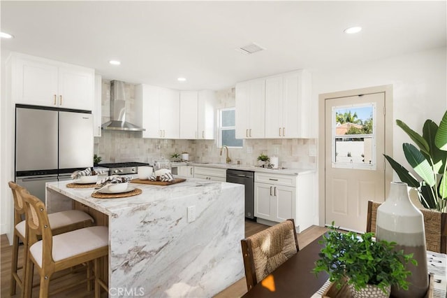 kitchen with a center island, white cabinets, wall chimney exhaust hood, appliances with stainless steel finishes, and light stone counters