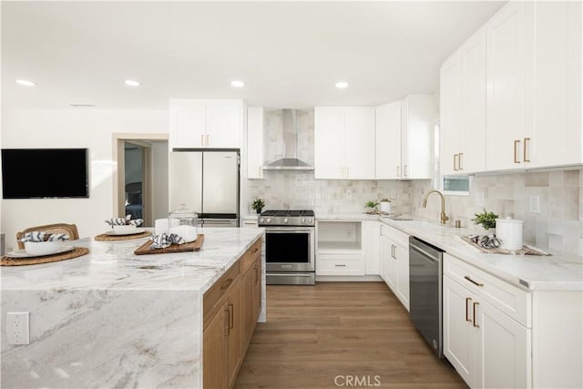 kitchen featuring wall chimney exhaust hood, sink, light stone counters, stainless steel appliances, and white cabinets