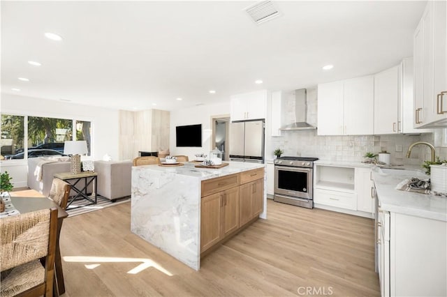 kitchen with white cabinetry, high end stainless steel range, sink, and wall chimney range hood