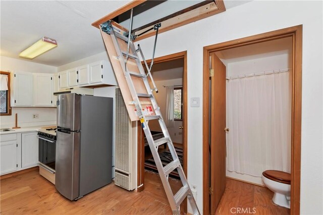 kitchen with stainless steel refrigerator, stove, white cabinets, and light hardwood / wood-style flooring