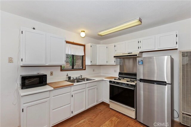 kitchen with light wood-type flooring, white gas range, sink, white cabinets, and stainless steel refrigerator