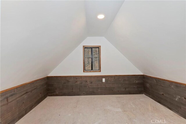 additional living space featuring vaulted ceiling and wooden walls