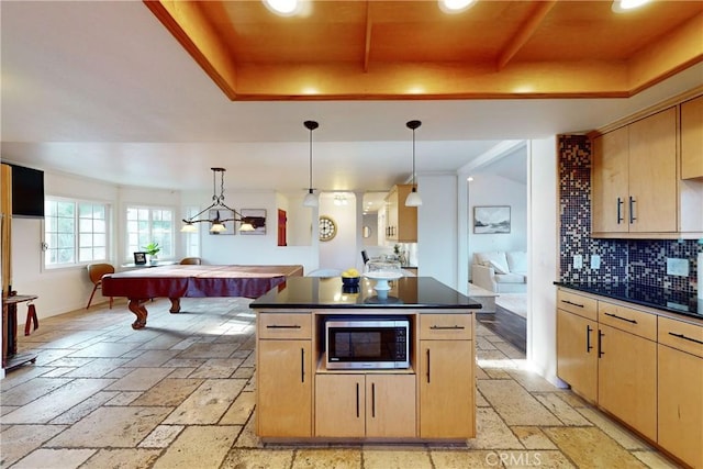 kitchen featuring stainless steel microwave, light brown cabinetry, hanging light fixtures, and a raised ceiling