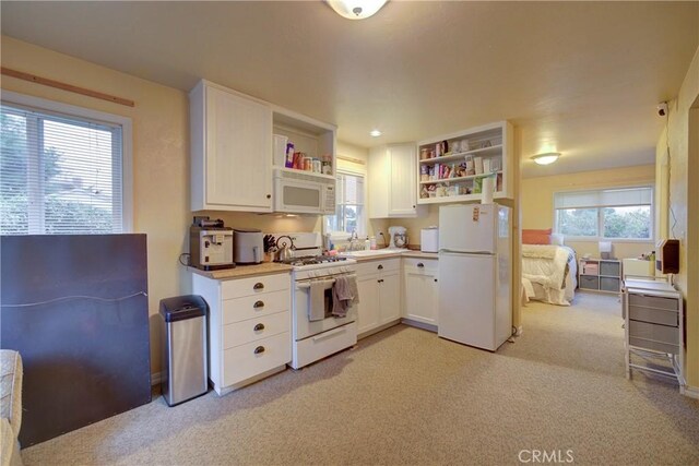 kitchen featuring white appliances, sink, light carpet, and white cabinets