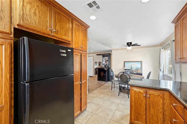 kitchen featuring ceiling fan, dark stone countertops, crown molding, black refrigerator, and light tile patterned floors