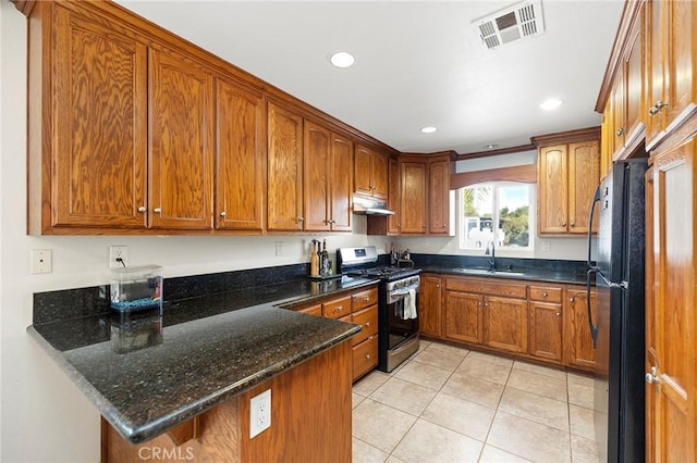 kitchen with dark stone counters, sink, gas range, light tile patterned floors, and kitchen peninsula