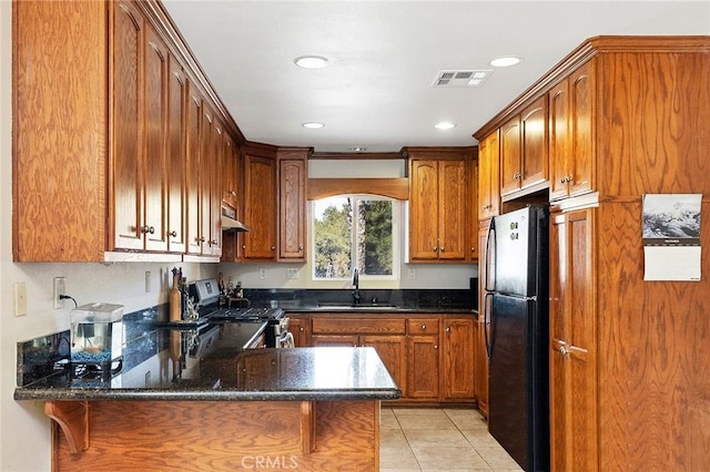 kitchen with black refrigerator, kitchen peninsula, sink, light tile patterned floors, and stainless steel electric range oven