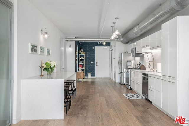 kitchen featuring tasteful backsplash, hardwood / wood-style floors, decorative light fixtures, white cabinets, and appliances with stainless steel finishes