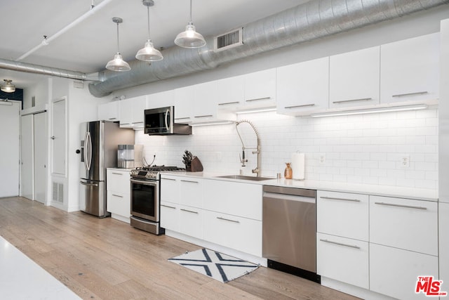 kitchen featuring pendant lighting, sink, light wood-type flooring, appliances with stainless steel finishes, and white cabinetry