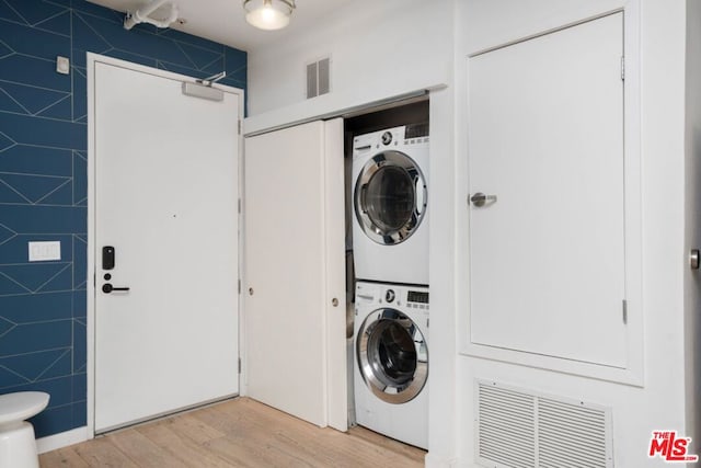 laundry area with light hardwood / wood-style flooring, stacked washing maching and dryer, and tile walls