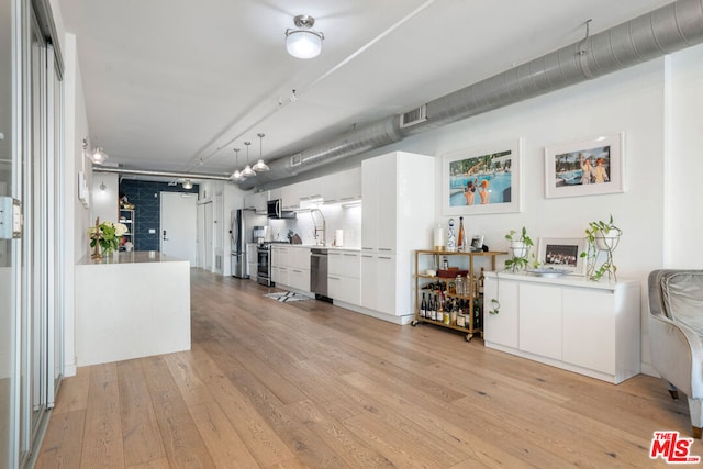 interior space with white cabinets, a fireplace, decorative light fixtures, light hardwood / wood-style floors, and stainless steel appliances