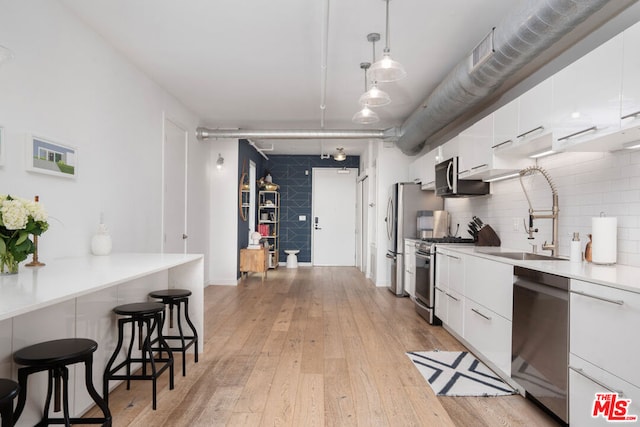 kitchen featuring appliances with stainless steel finishes, sink, pendant lighting, white cabinets, and light hardwood / wood-style floors