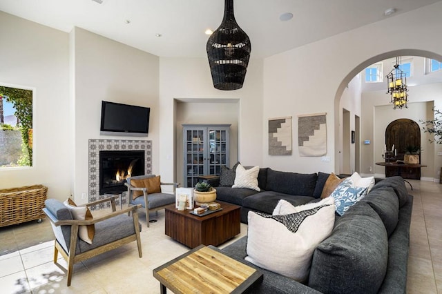 tiled living room featuring a fireplace, a towering ceiling, and a chandelier