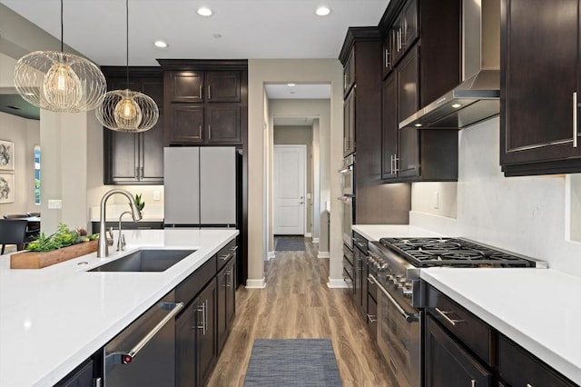 kitchen featuring pendant lighting, wall chimney range hood, sink, stainless steel appliances, and dark brown cabinetry