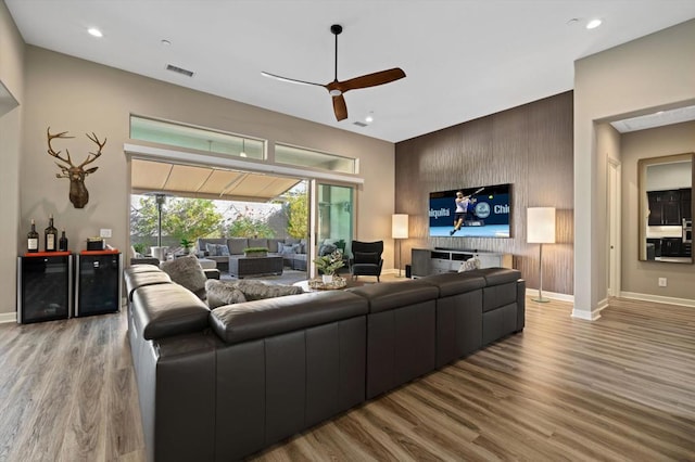 living room with ceiling fan, wine cooler, wooden walls, and light hardwood / wood-style flooring